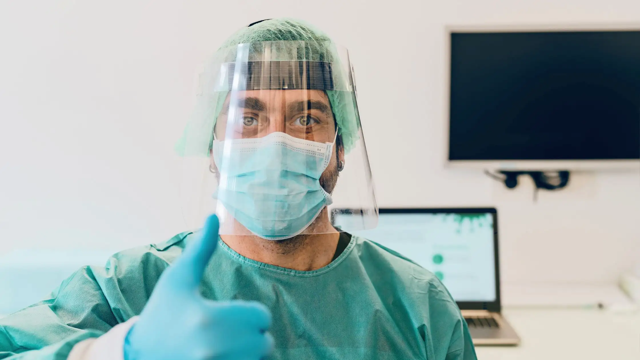 hospital staff in scrubs, face mask, and face shield giving a thumbs up